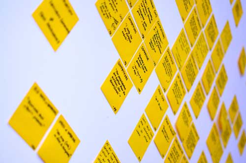 A wall covered in yellow post-it notes with user research quotes written on them